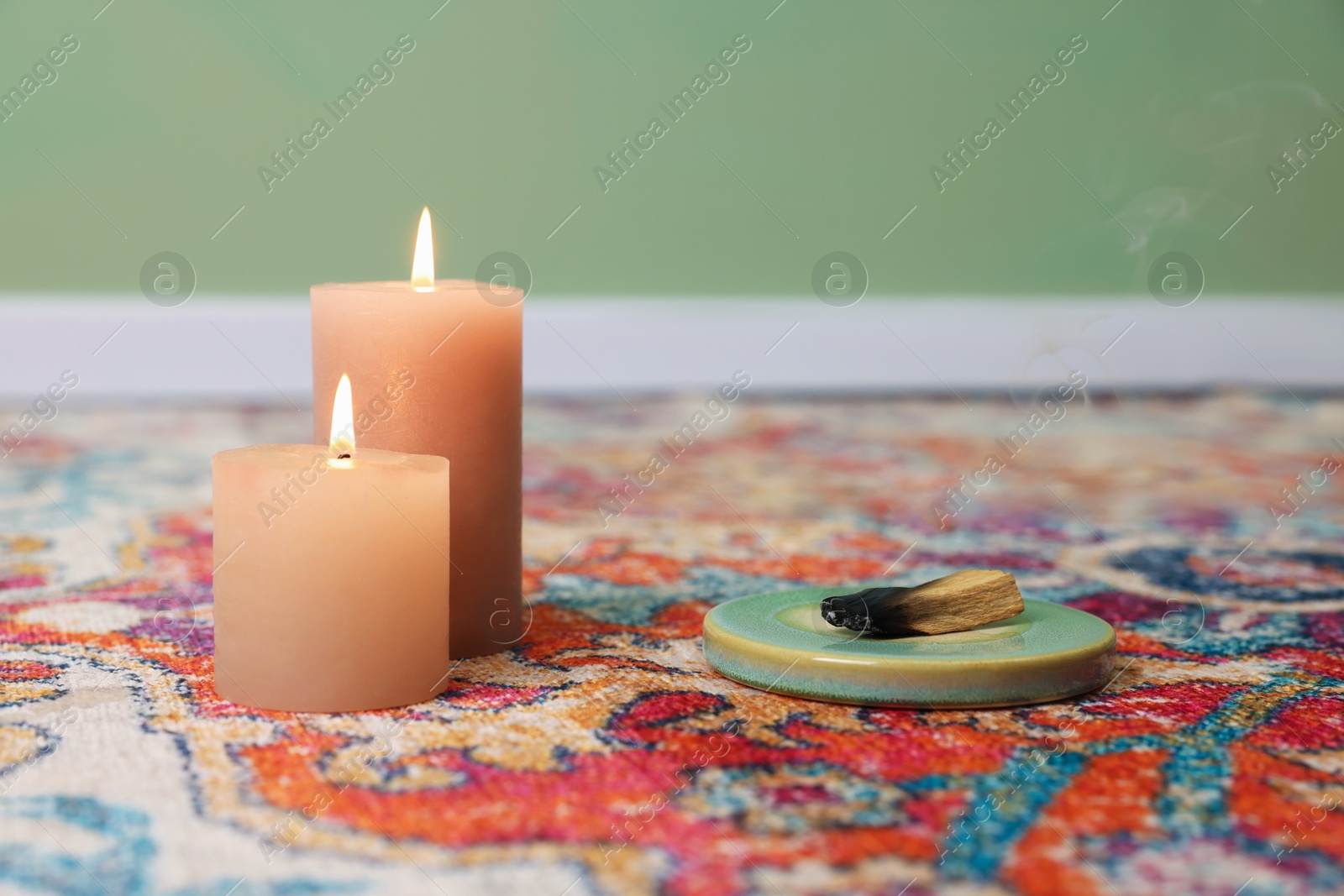 Photo of Palo santo sticks and burning candles on rug indoors, space for text