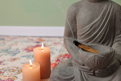 Photo of Buddha statue with palo santo sticks and burning candles indoors, closeup. Space for text