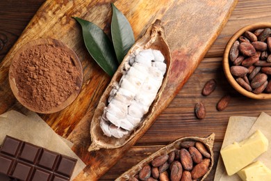 Photo of Cocoa pods with beans, chocolate and butter on wooden table, flat lay