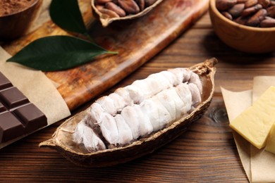 Photo of Cocoa pod with beans, chocolate and butter on wooden table, closeup