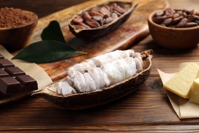 Photo of Cocoa pods with beans, chocolate and butter on wooden table, closeup