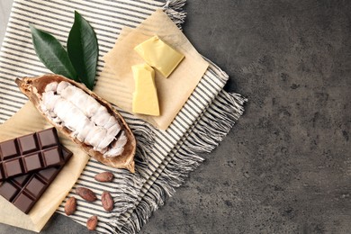 Cocoa pod with beans, butter and chocolate on grey table, flat lay. Space for text