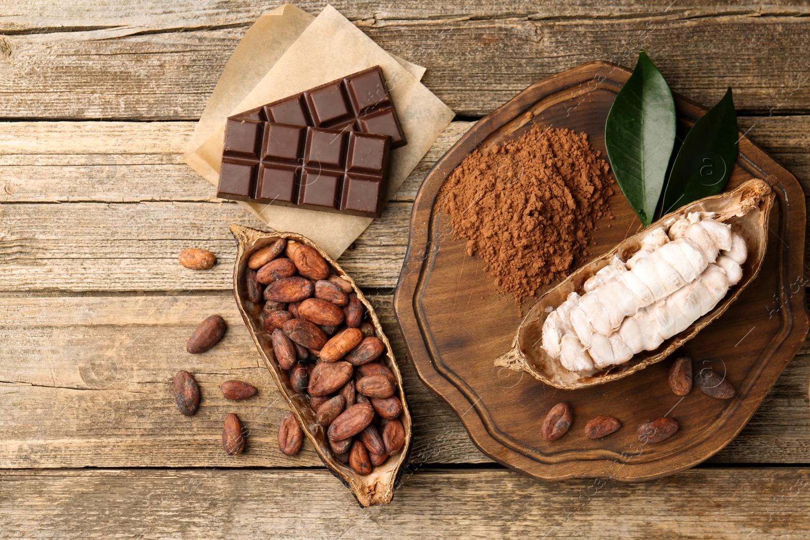 Cocoa pods with beans, powder and chocolate on wooden table, flat lay Photo of Cocoa pods with beans, powder and chocolate on wooden table, flat lay