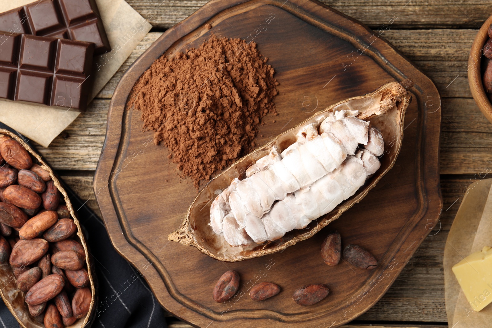 Photo of Cocoa pods with beans, powder, chocolate and butter on wooden table, flat lay