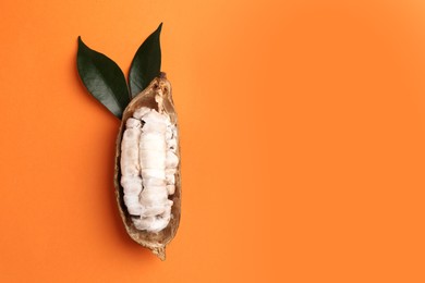 Photo of Cocoa pod with beans on orange background, top view. Space for text