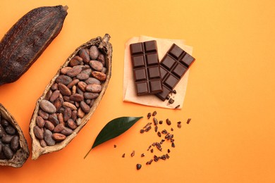 Photo of Cocoa pods with beans and chocolate on orange background, flat lay