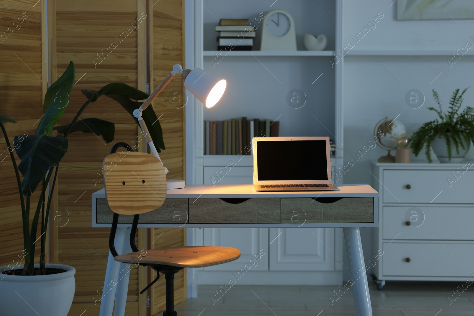 Photo of Comfortable workplace with laptop and lamp on table indoors