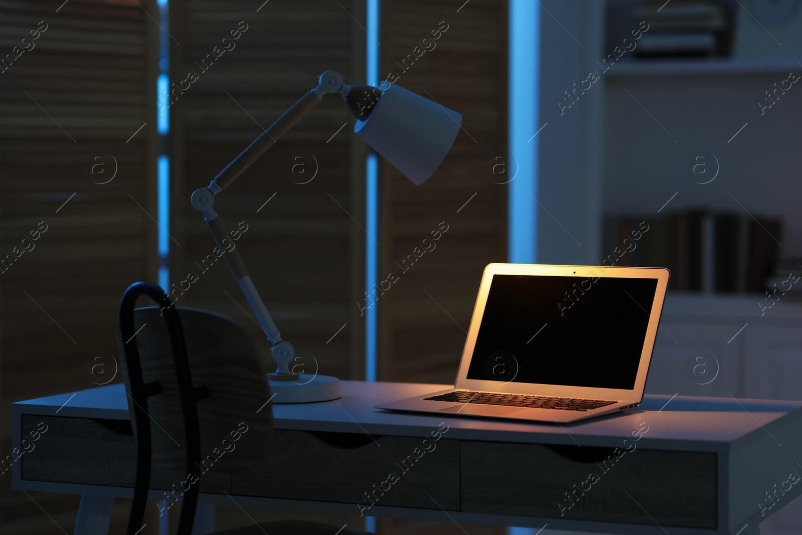 Photo of Comfortable workplace with laptop and lamp on table indoors