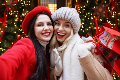 Happy friends with shopping bags taking selfie on city street. Christmas season