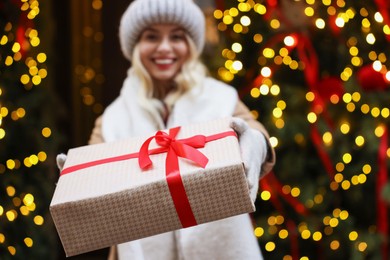 Photo of Happy woman with Christmas gift on city street, selective focus. Space for text