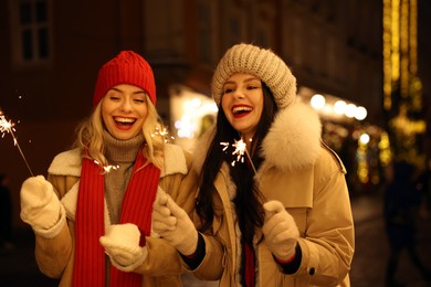 Photo of Happy friends with sparklers on city street. Christmas season