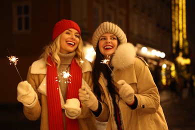 Photo of Happy friends with sparklers on city street. Christmas season