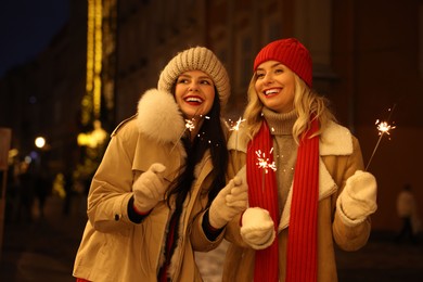 Photo of Happy friends with sparklers on city street. Christmas season