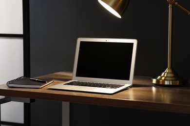 Photo of Home office. Comfortable workplace with laptop and lamp on wooden desk indoors