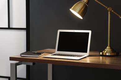 Photo of Home office. Comfortable workplace with laptop and lamp on wooden desk indoors