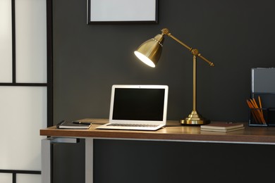 Photo of Home office. Comfortable workplace with laptop and lamp on wooden desk indoors