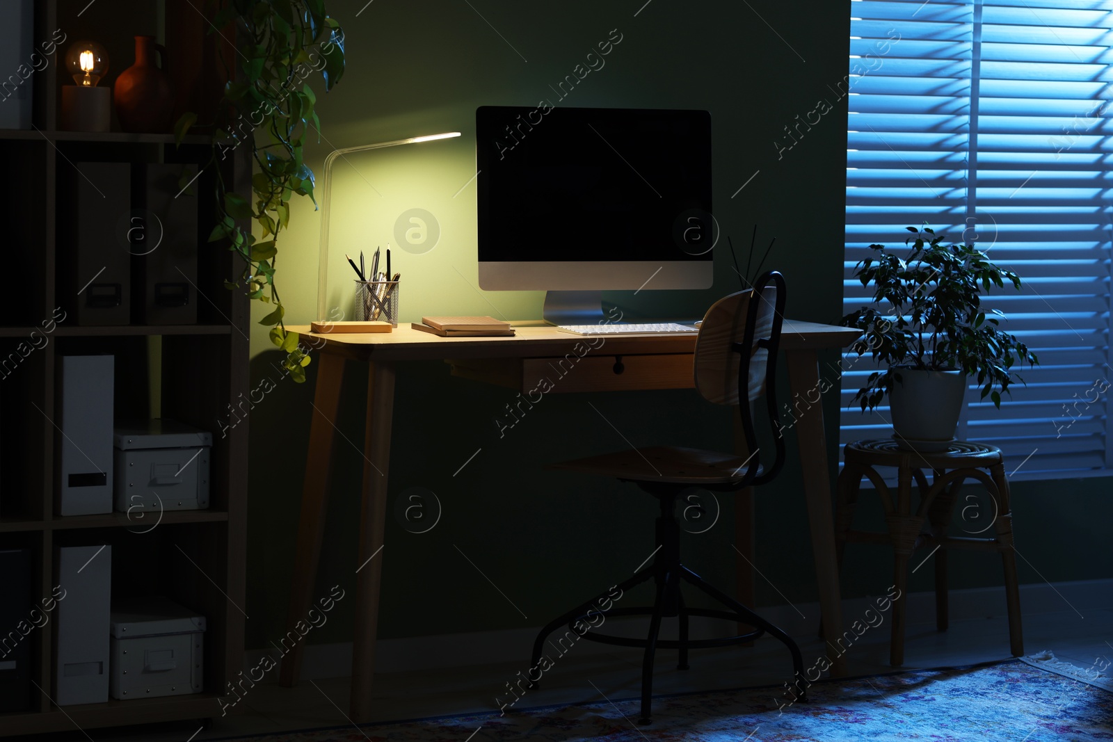 Comfortable workplace with computer and lamp on wooden desk at home office in evening Photo of Comfortable workplace with computer and lamp on wooden desk at home office in evening