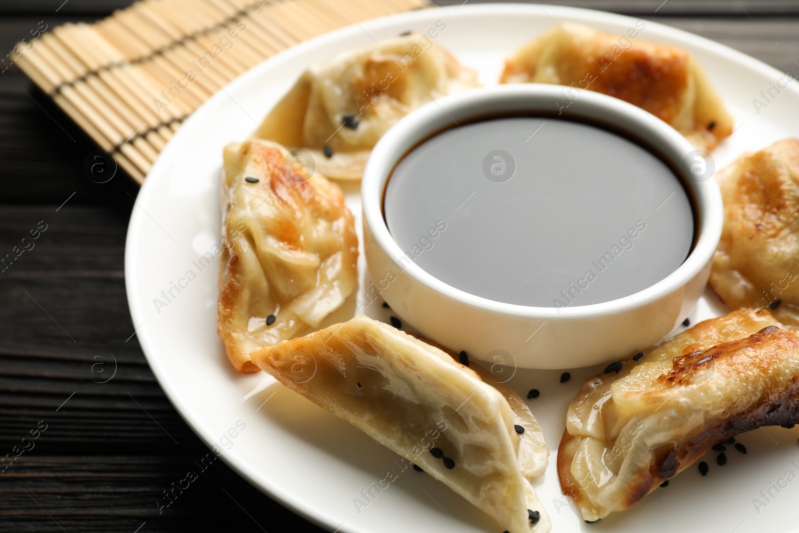 Photo of Delicious fried gyoza dumplings with sesame seeds and soy sauce on wooden table, closeup