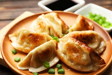 Photo of Delicious fried gyoza dumplings with green onions served on wooden table, closeup