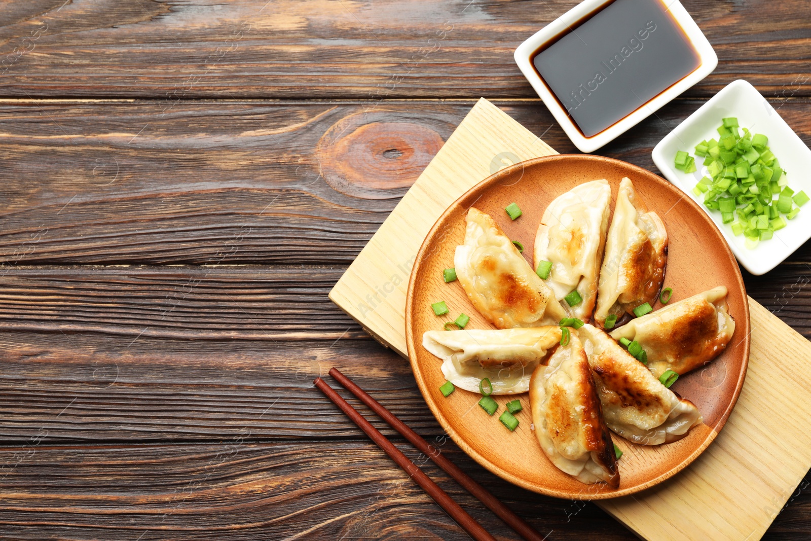 Photo of Delicious fried gyoza dumplings with green onions served on wooden table, flat lay. Space for text