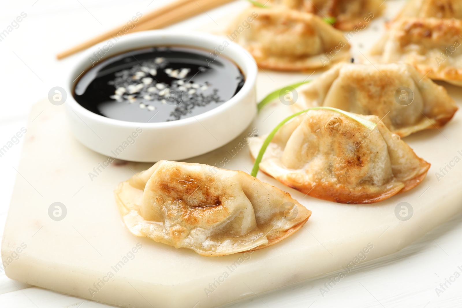 Photo of Fried gyoza dumplings with soy sauce on white table, closeup