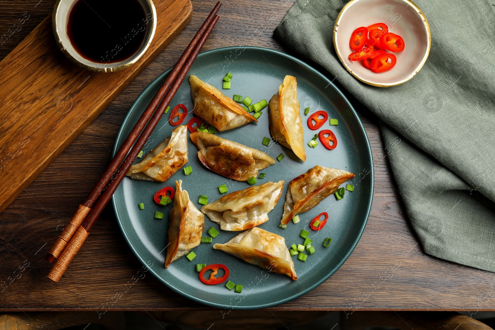 Photo of Delicious fried gyoza dumplings with green onions and chili peppers served on wooden table, flat lay