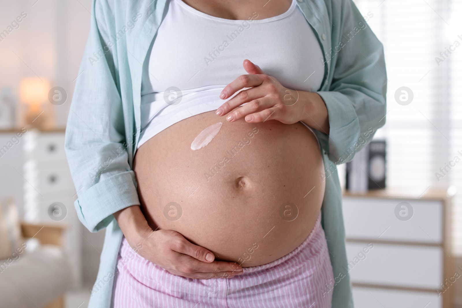 Photo of Pregnant woman applying cream on belly at home, closeup