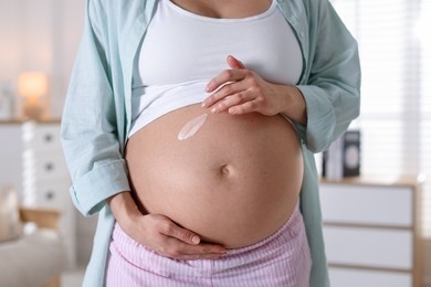 Photo of Pregnant woman applying cream on belly at home, closeup