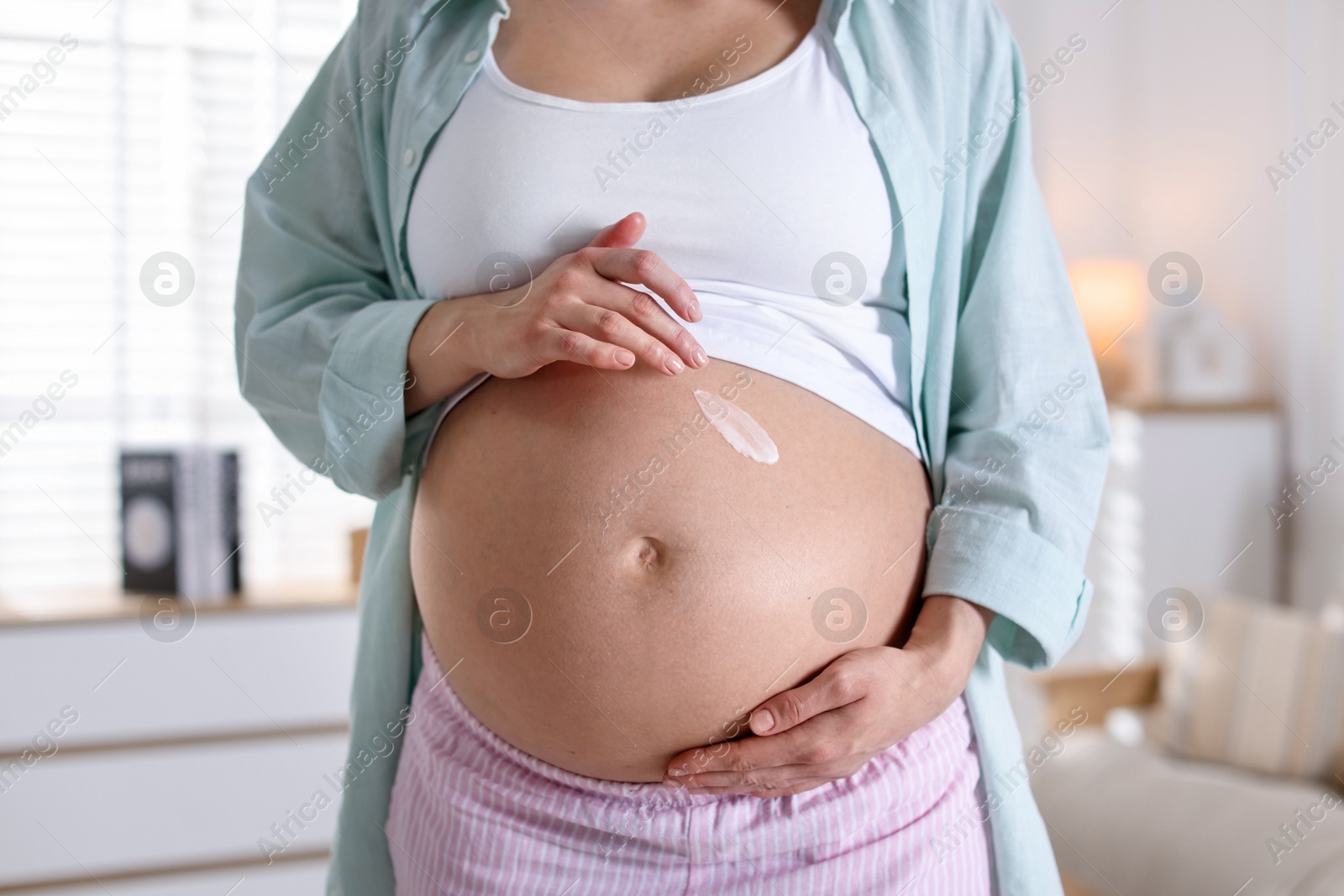 Photo of Pregnant woman applying cream on belly at home, closeup