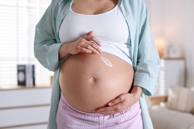 Photo of Pregnant woman applying cream on belly at home, closeup