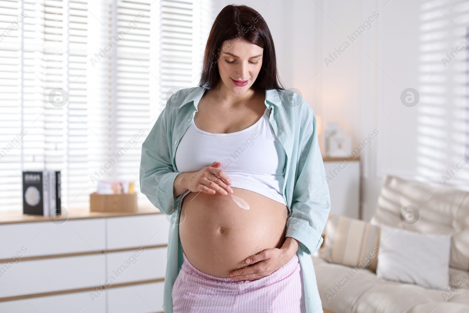 Photo of Beautiful pregnant woman applying cream on belly at home