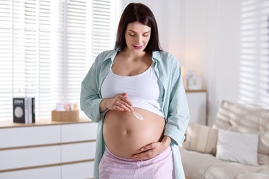 Photo of Beautiful pregnant woman applying cream on belly at home