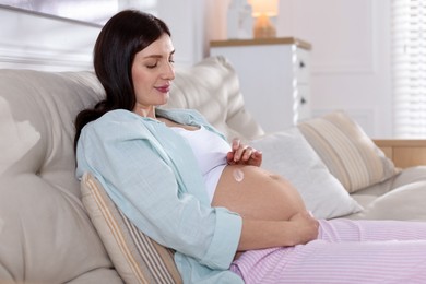 Photo of Beautiful pregnant woman applying cream on belly at home