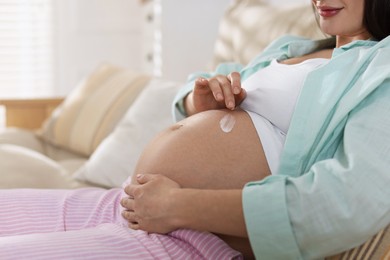 Photo of Pregnant woman applying cream on belly at home, closeup