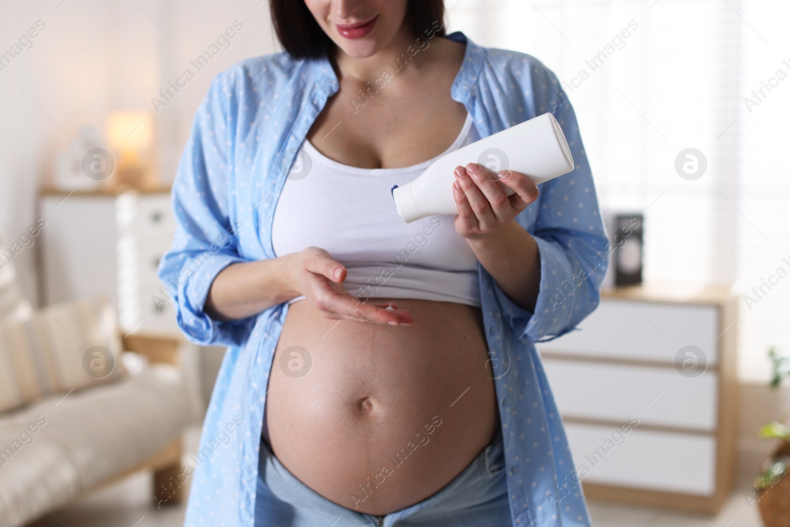 Photo of Pregnant woman applying cream on belly at home, closeup