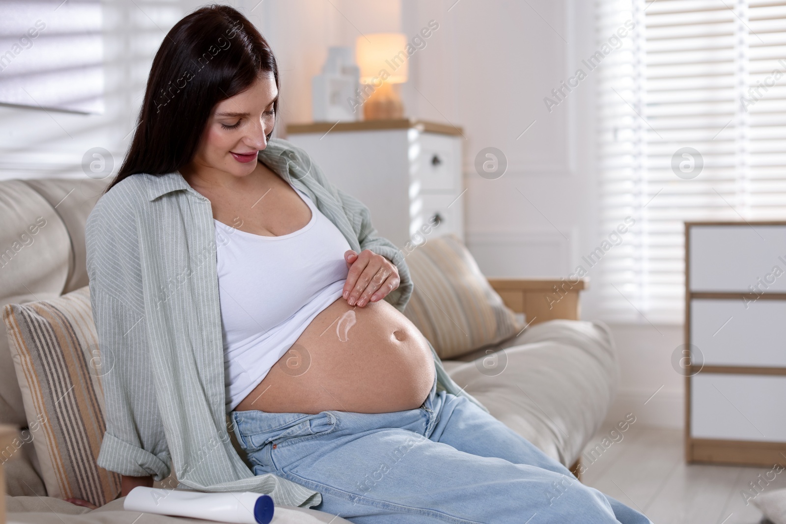 Photo of Beautiful pregnant woman applying cream on belly at home