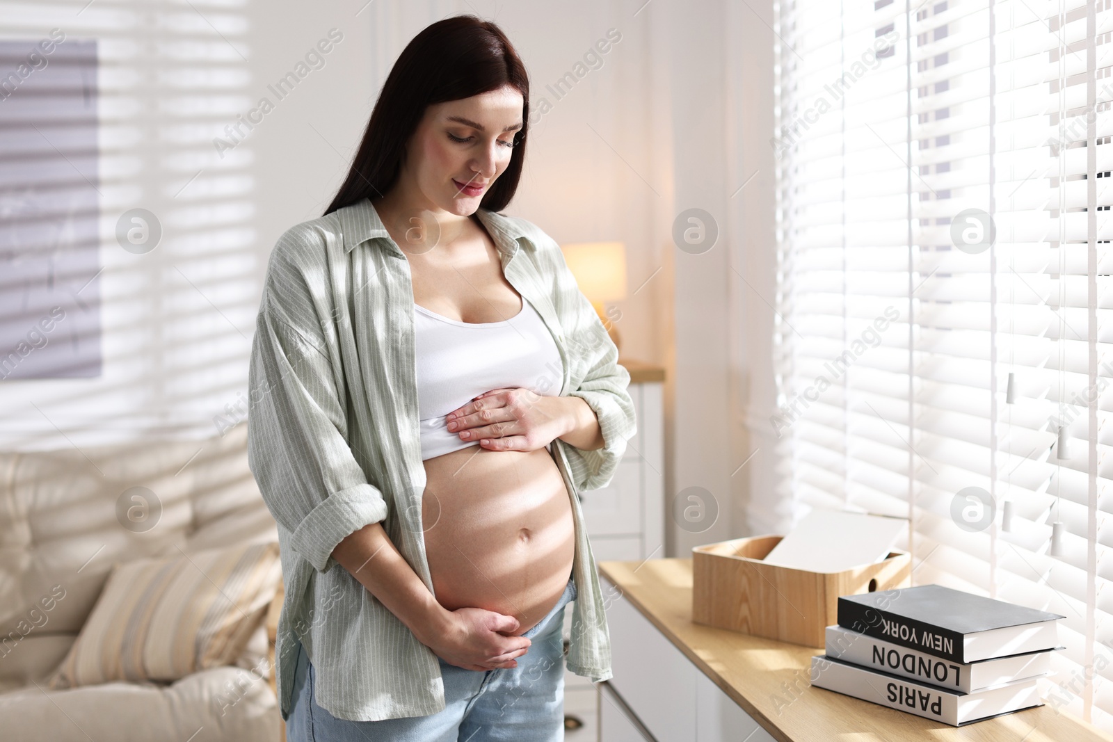 Photo of Beautiful pregnant woman with cute belly near window at home