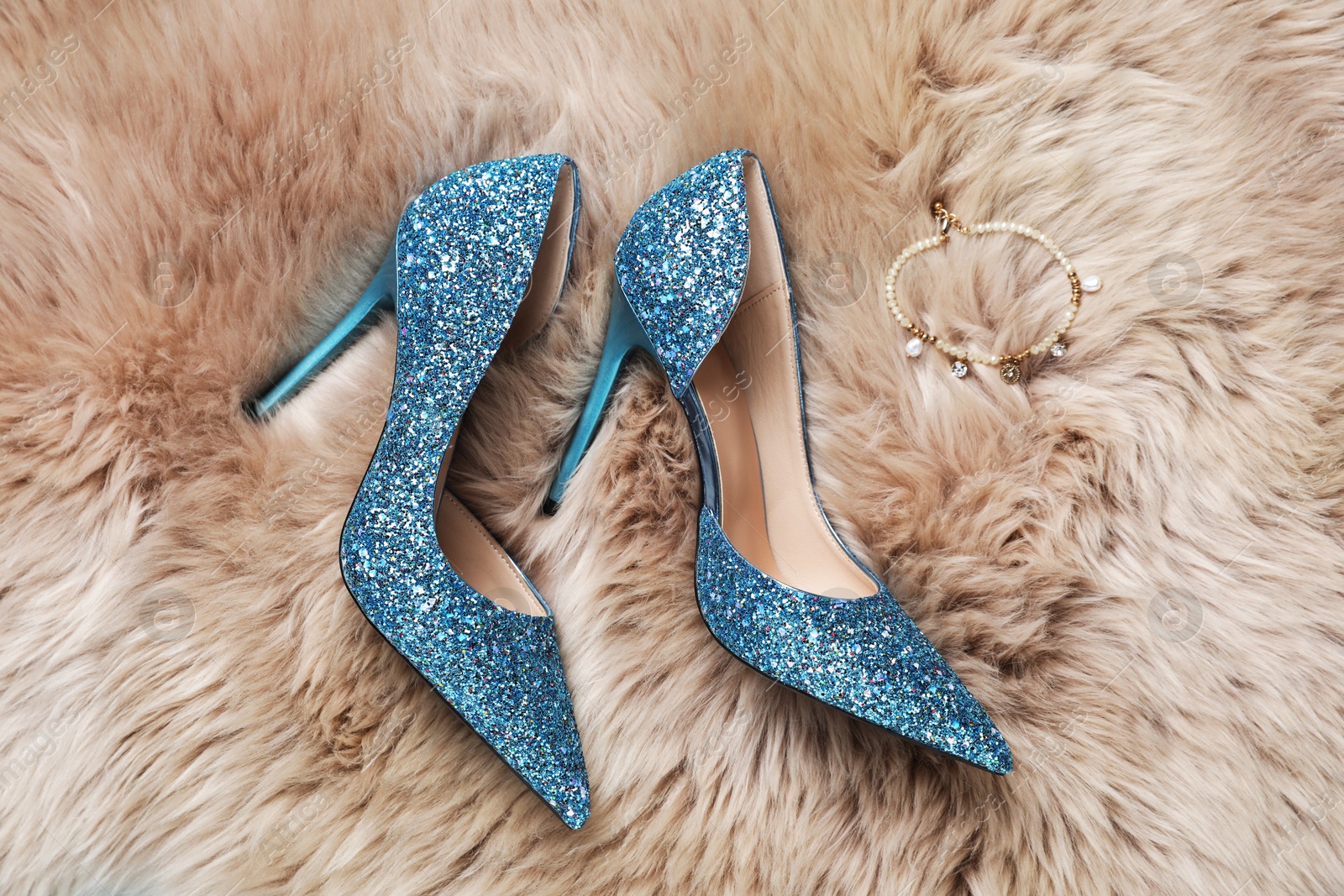 Photo of Beautiful high heeled shoes and bracelet on faux fur, flat lay