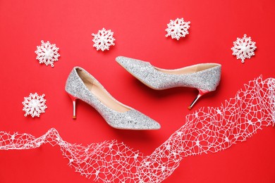 Beautiful high heeled shoes, decorative snowflakes and lace ribbon on red background, flat lay