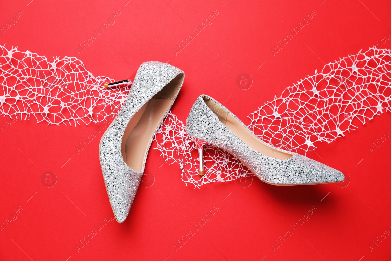 Photo of Beautiful high heeled shoes, and lace ribbon on red background, flat lay