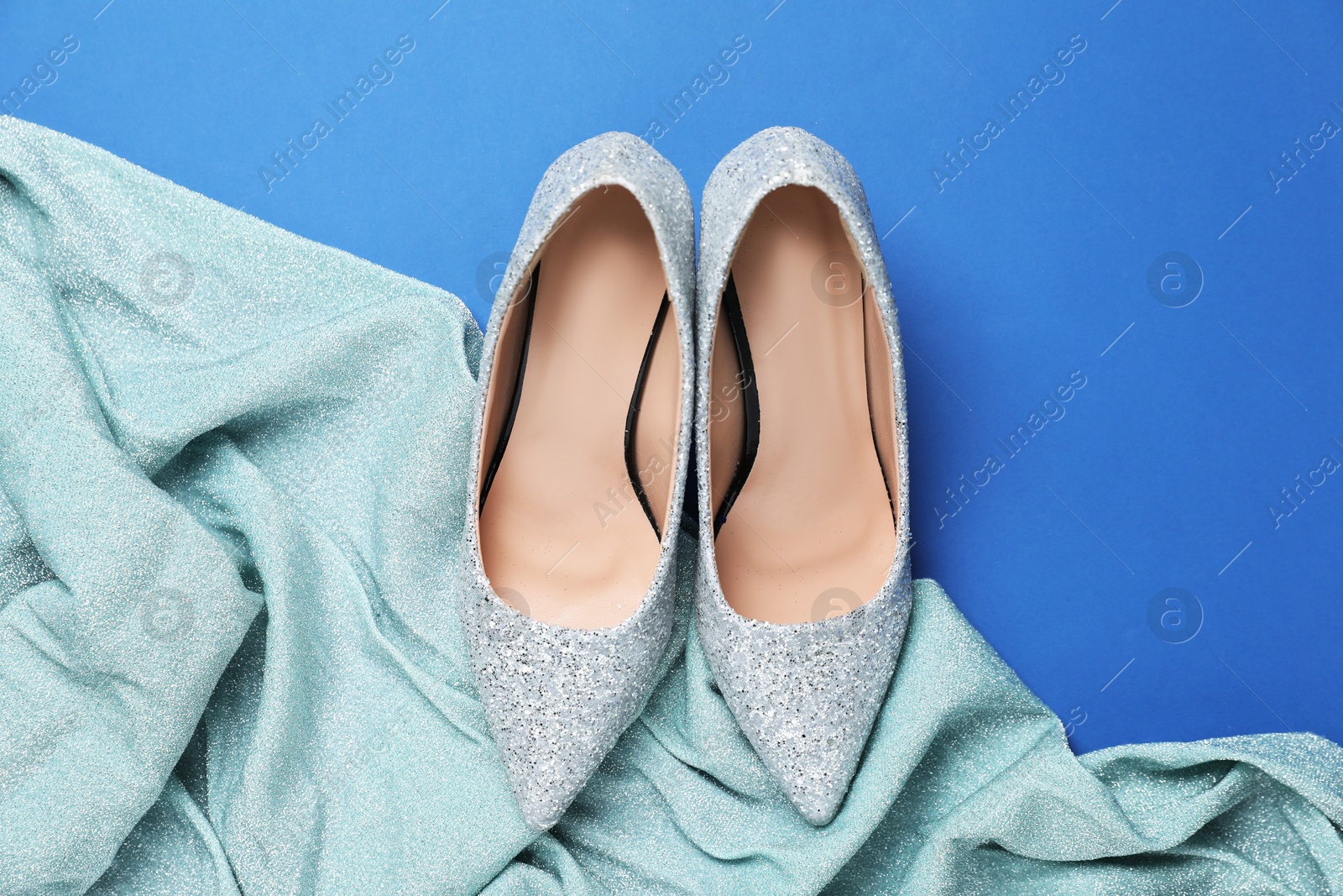 Photo of Beautiful high heeled shoes and shiny cloth on blue background, flat lay