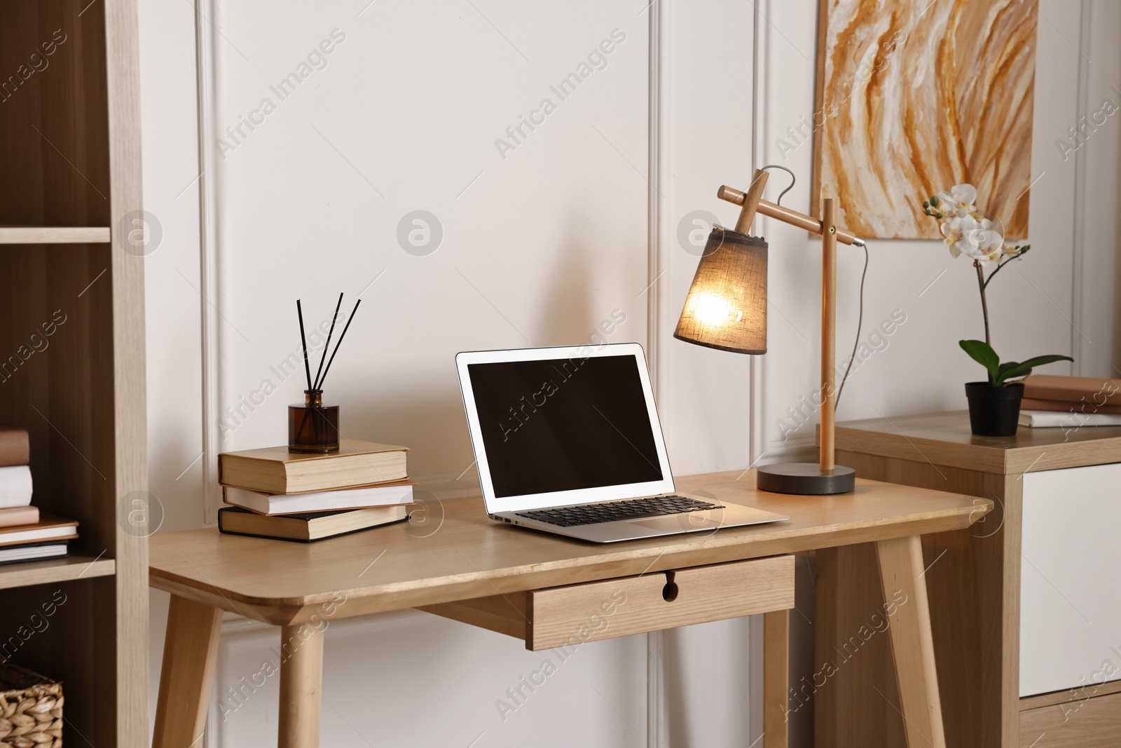 Comfortable workplace with modern laptop and lamp on wooden desk in home office Photo of Comfortable workplace with modern laptop and lamp on wooden desk in home office