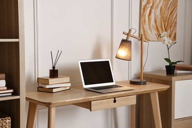 Photo of Comfortable workplace with modern laptop and lamp on wooden desk in home office