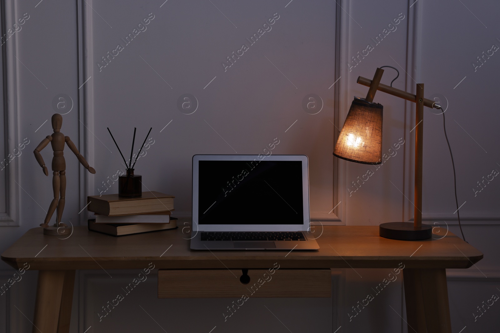 Comfortable workplace with modern laptop and lamp on wooden desk at home office in evening Photo of Comfortable workplace with modern laptop and lamp on wooden desk at home office in evening