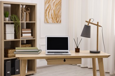 Photo of Comfortable workplace with modern laptop and lamp on wooden desk in home office