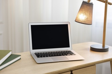 Photo of Comfortable workplace with modern laptop and lamp on wooden desk in home office