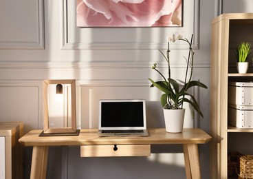 Photo of Comfortable workplace with modern laptop and lamp on wooden desk in home office