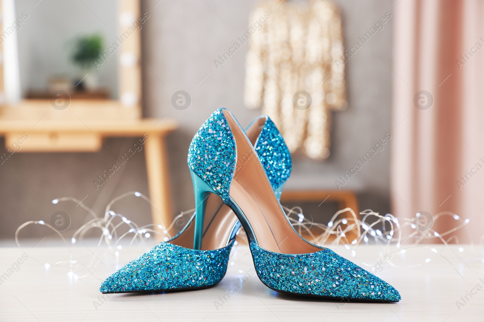 Photo of Elegant high heeled shoes and festive lights on white wooden table indoors