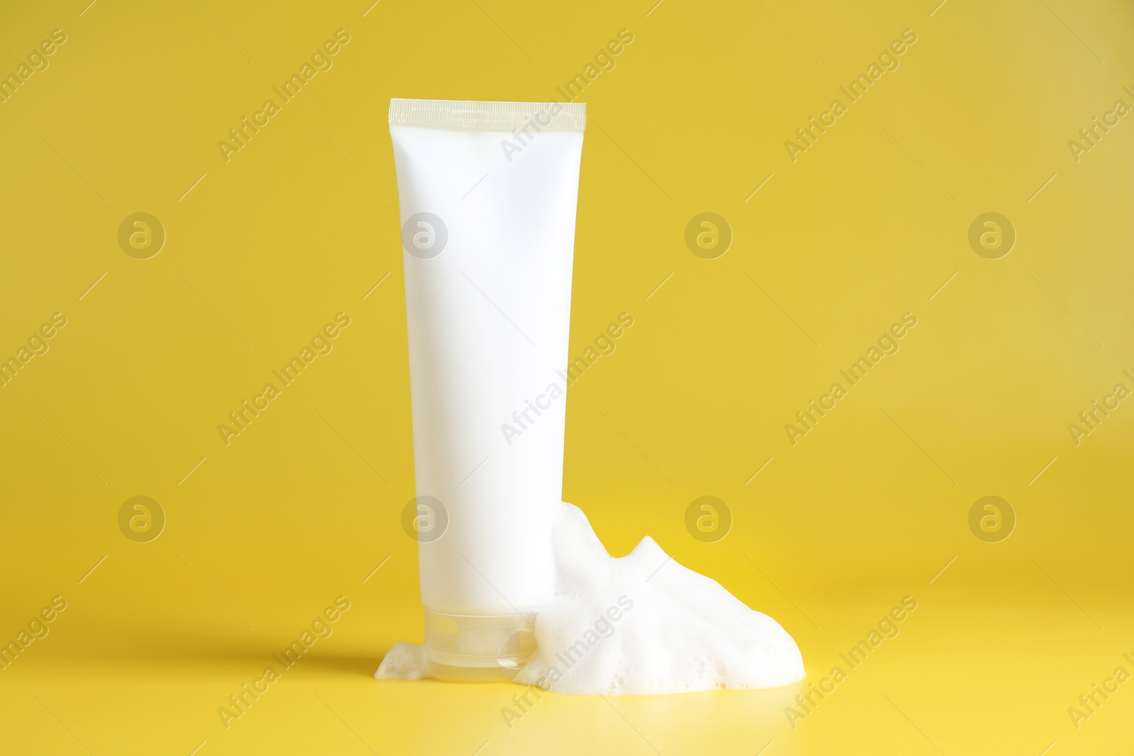 Photo of Tube of cosmetic product with foam on yellow background