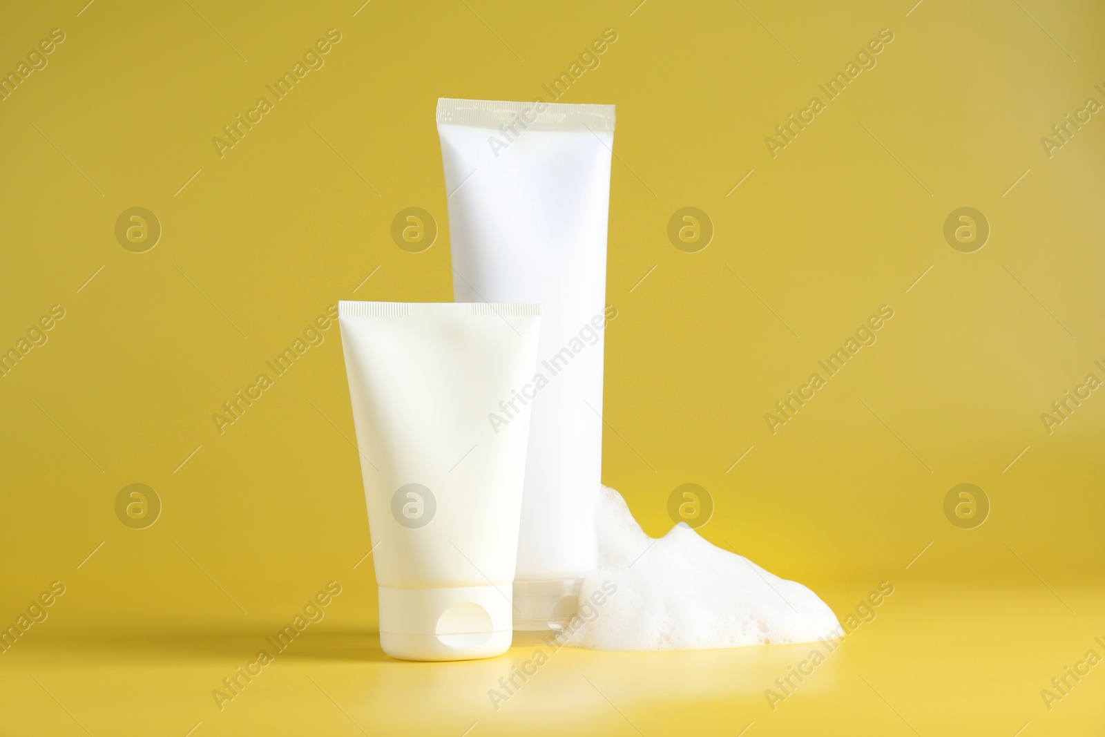 Photo of Tubes of cosmetic products with foam on yellow background